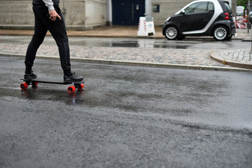 A business man rides an electric skateboard along the street in rainy weather. The concept of portable personal transport. © Oleksandr