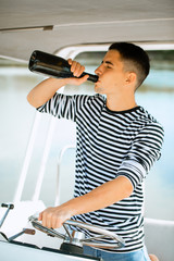 A man sailing in the sea on a boat on a sunny day and drink alcochol.
