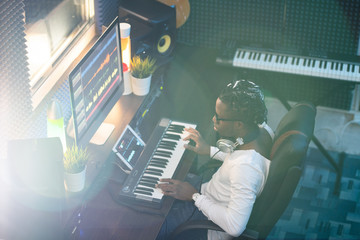 Young African musician in casualwear looking at computer screen by workplace
