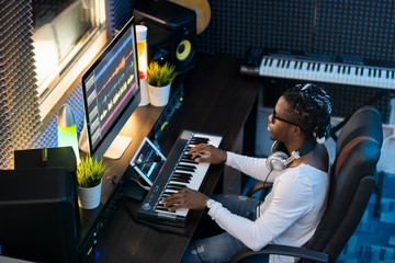 Young musician of African ethnicity sitting by workplace in studio of recording