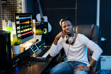 Young successful African man in casualwear sitting by workplace in studio