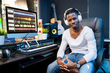 Happy young successful musician or producer in headphones sitting by workplace