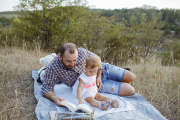 Dad and his daughter are reading books at sunset.