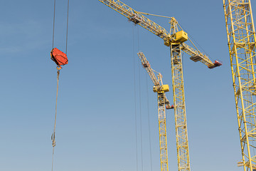 Naklejka premium Several yellow high-rise construction cranes build multi-storey multi-apartment residential buildings using modern technologies of metal, concrete and brick according to the architectural design