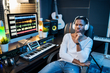 Young serious African musician in casualwear and headphones sitting in armchair