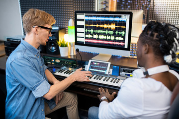 Two young multicultural musicians discussing new way of mising sounds in studio