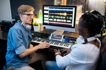 Multi-ethnic musicians in casualwear sitting by workplace in recording studio