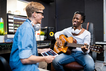 Happy African man with guitar and his colleague working over new soundtrack