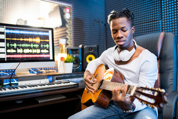 Contemporary young musician or guitarist in casualwear playing guitar in studio