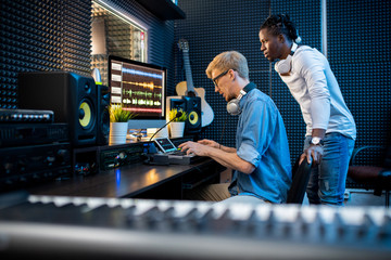 One of young musicians pressing pianoboard keys with colleague standing near by