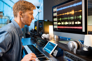 Serious man touching one of pianoboard keys while looking at sound waveforms