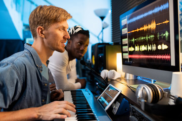 Young man with pianoboard looking at computer screen during work in studio