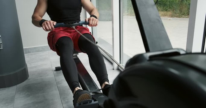 Strong Muscular male working on indoor rower simulator. Cross Fitness Training in the gym