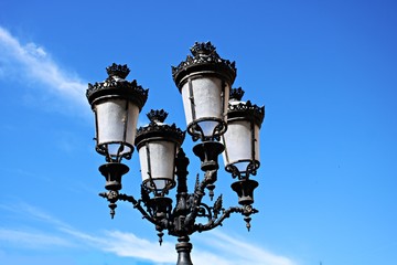 Fototapeta na wymiar Beautiful old metal street lamp post with four lamps on a blue sky background