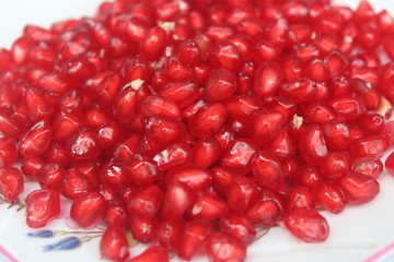 Pomegranate seeds placed in a plate with scattered seeds on white background