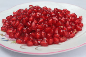 Pomegranate seeds placed in a plate with scattered seeds on white background
