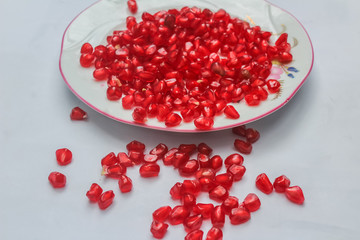Pomegranate seeds placed in a plate with scattered seeds on white background