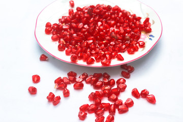 Pomegranate seeds placed in a plate with scattered seeds on white background