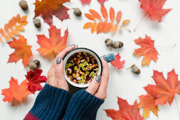 Female hands holding tea over table with red maple and rowan leaves and acorns