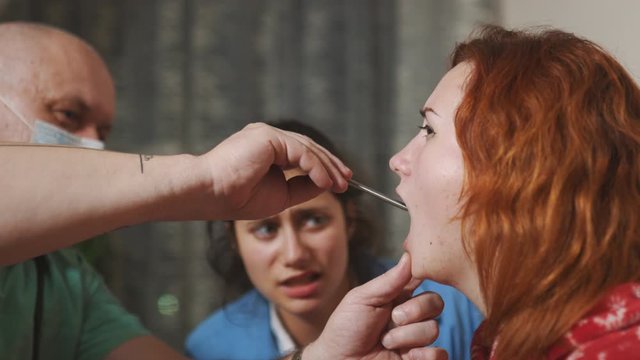 Sick caughing woman getting her diagnosis by an ambulance doctor teaching a medical student intern - Ill patient with flu called young doctor for examination and checkup