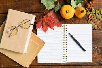 Open copybook with pen, books with eyeglasses, pumpkins and autumn leaves