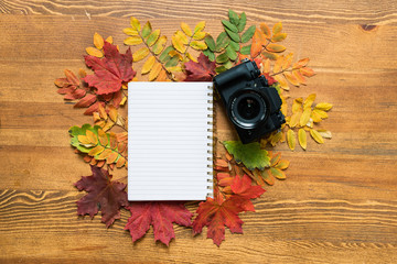 Blank sheet of copybook surrounded by colorful autumn leaves with photocamera