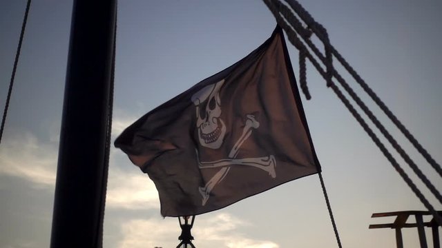 Black pirate flag waving in slow motion on a ship.