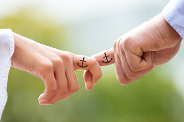 Close-up Of Couple Holding Index Fingers With Anchor Sign