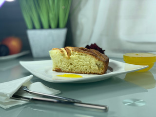 Charlotte apple, on a white plate. Cutlery for food. Breakfast indoors. Honey, decorative flowers on the table.