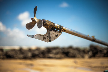 Boat propeller in the background, beach landscape with rocks and sand.
