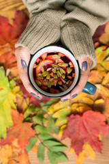 Female hands holding mug of hot herbal tea with lemon over autumn leaves