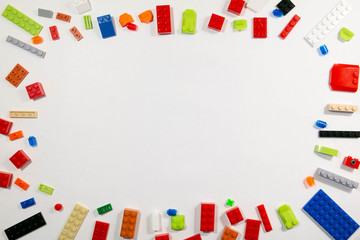 Colorful children`s background from cubes the designer. Frame from kid's toys on a white backdrop. Plastic blocks laid out at the edges and an empty space in a middle. Top view, flat lay.