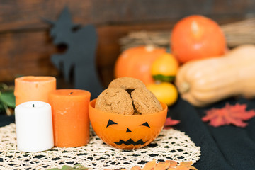 Halloween plastic bowl with cookies and three candles on white knitted napkin
