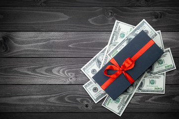 Black gift box with bow with dollars banknotes on dark wooden backgroung. top view