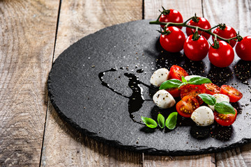 Caprese salad on black stone plate on wooden table