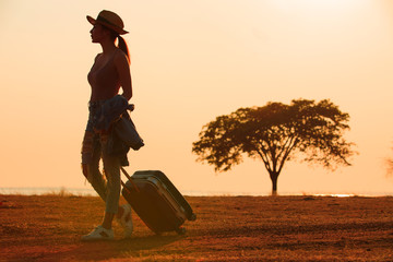 The silhouette of a sexy woman walking a drag on a road bag against a beautiful lake background, a female tourist with a nature trip at sunset