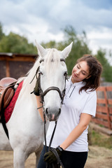 Young woman cuddling white racehorse and looking at her while chilling out