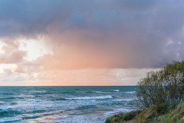 It rains over the sea, which is illuminated by sunset.