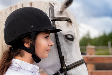 Profile of young active woman in equestrian helmet and white purebred horse