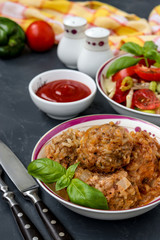 Meatballs in sour cream sauce and fresh vegetable salad in bowls against a dark background, vertical orientation