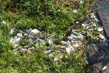 Naklejka na ściany i meble Closeup of bottles, bags and plastic trash floating in the water of Rio Tapajos surrounded by natural vegetation. Environment, pollution, plastic free, trash, recycling and conservation concept.
