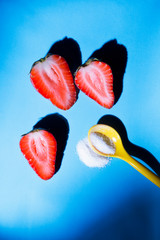 Top view on three halved strawberries and a spoonful of sugar