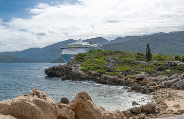 Large cruise ship emerging behind rocky outcrop.