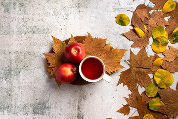 Autumn composition. Red apples, cup of tea, leaves, on  gray concrete background. Flat lay.