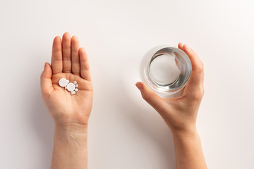 Healthcare and medical concept. Person holding pills in one hand and glass of water in the another...