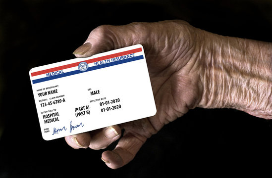 An elderly female hand holds a mock United State government Medicare Health Insurance card. It is a generic card.