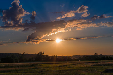Fototapeta premium Rural landscape at sunset, clouds, fields, countryside, flares, grain in front, nature
