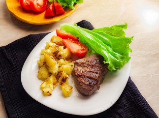 Hot steak on white dish with fried potates and fresh vegetables