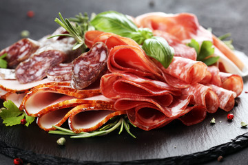 Marble cutting board with prosciutto, bacon, salami and sausages on wooden background. Rustic Meat platter