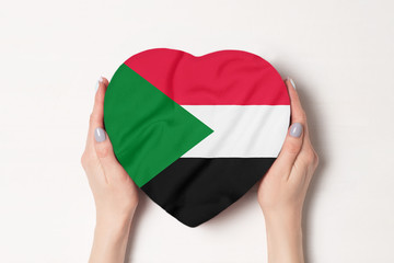 Flag of Sudan on a heart shaped box in a female hands. White background